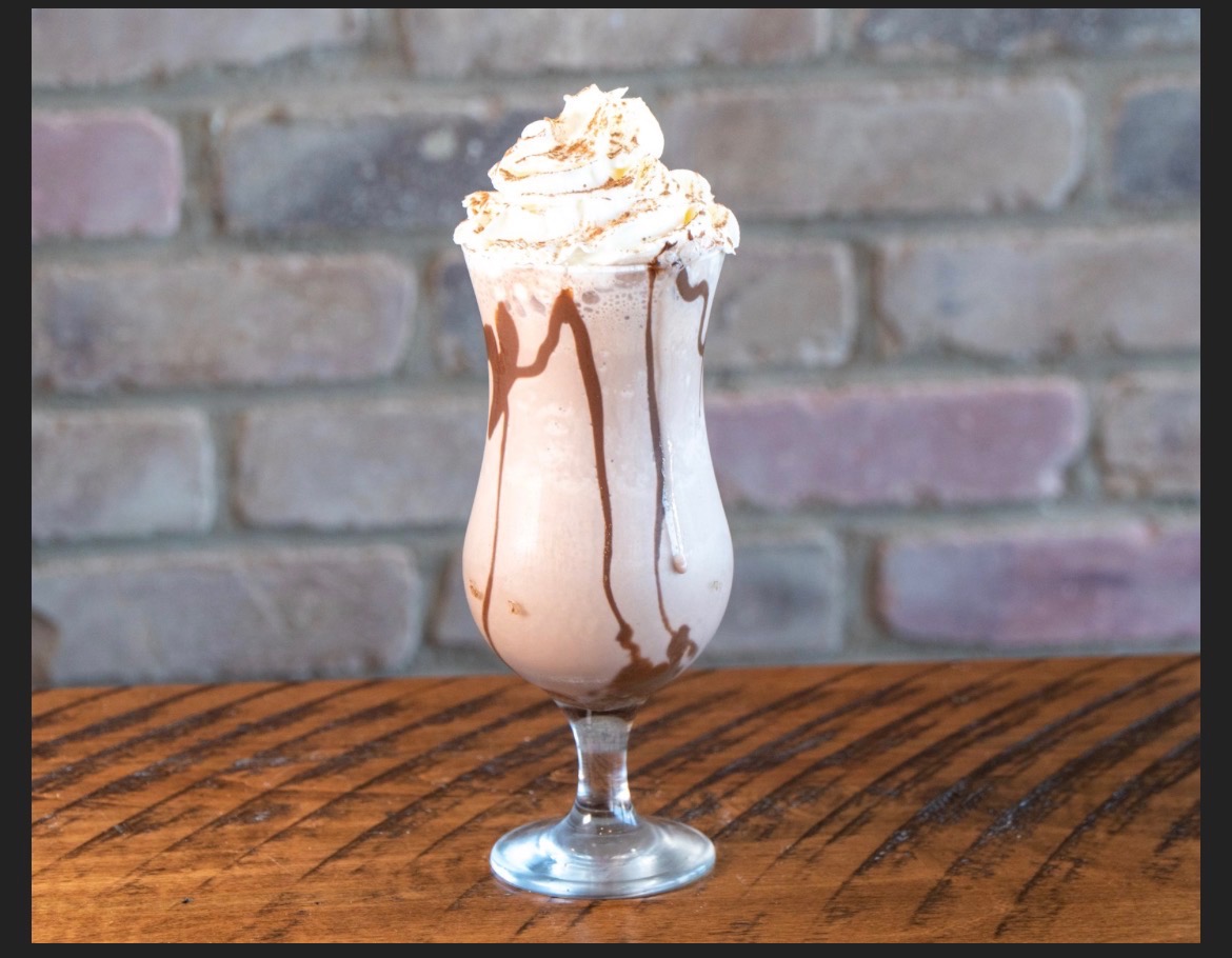 Thick chocolate milkshake in a tall glass topped with whipped cream and chocolate drizzle