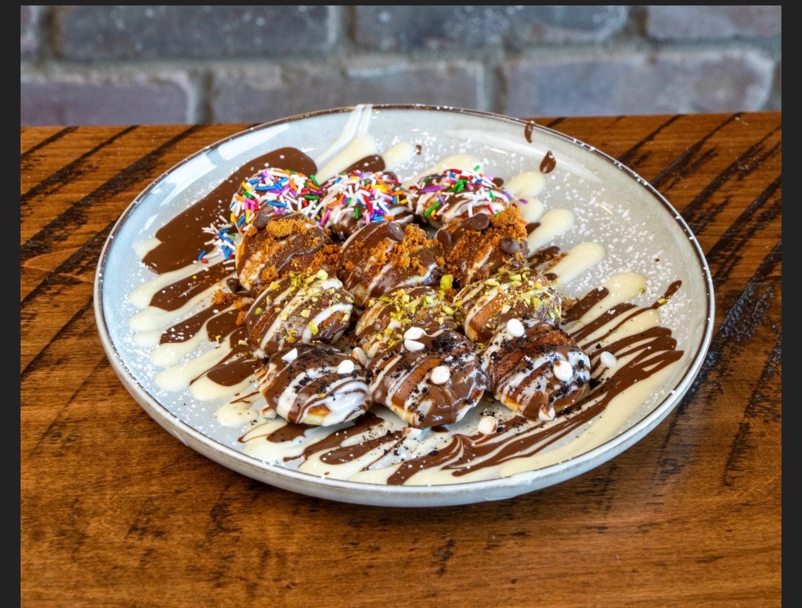 Mini Dutch pancakes topped with sprinkles, chocolate, pistachio and drizzle